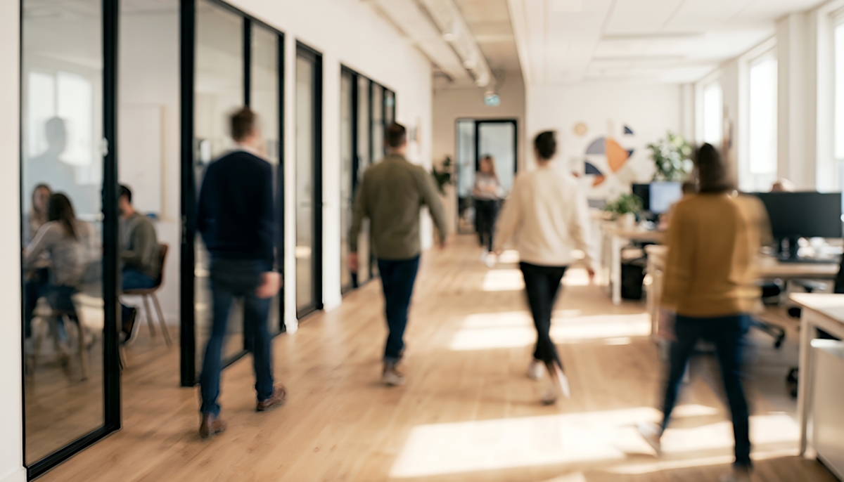 Eine Gruppe von Menschen, die durch ein modernes Büro mit Glaswänden geht, das eine kollaborative Arbeitsumgebung und Tageslicht zeigt.
